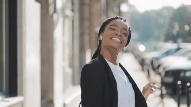Genç mutlu Afro-Amerikan iş kadını kulaklıkla şehir caddesinde yürürken akıllı telefondan müzik dinlerken, komik dans. ve kameraya bakarak. Açık.