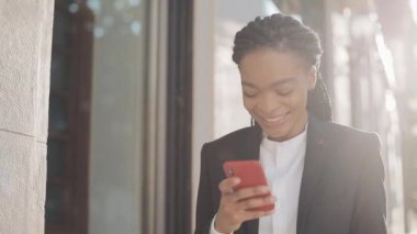 Şık afro iş kadını iş merkezi yakınında sokakta duran akıllı telefon kullanarak. Siyah Şık. Dreadlocks. Takım elbiseli kadın profesyonel akıllı telefonda iyi haberler.