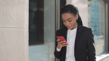 Şık afro iş kadını iş merkezi yakınında sokakta duran akıllı telefon kullanarak. Siyah Şık. Dreadlocks. Takım elbiseli kadın profesyonel akıllı telefonda iyi haberler.