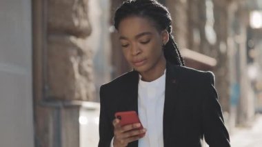Yorgun iş kadını iş merkezi yakınında sokakta yürüyen akıllı telefon kullanarak. Siyah Şık. Dreadlocks.