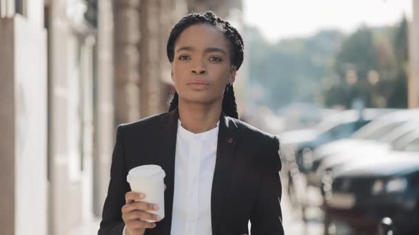 Портрет серьезной афроамериканской бизнесвумен в костюме, гуляющей по городу и пьющей кофе. Концепция: новый бизнес, рабочий день, фрилансер . — стоковое видео