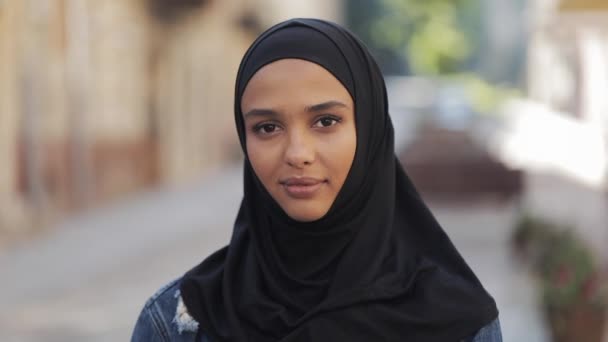 Retrato de una hermosa joven musulmana con pañuelo en la cabeza hijab sonriendo a la cámara de pie sobre el fondo de la vieja ciudad . — Vídeo de stock