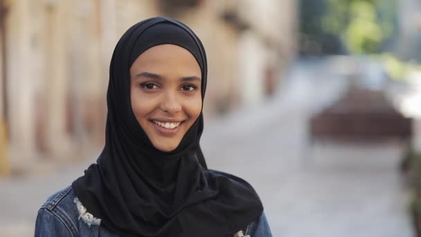 Retrato de una hermosa joven musulmana con pañuelo en la cabeza hijab sonriendo a la cámara de pie sobre el fondo de la vieja ciudad . — Vídeo de stock