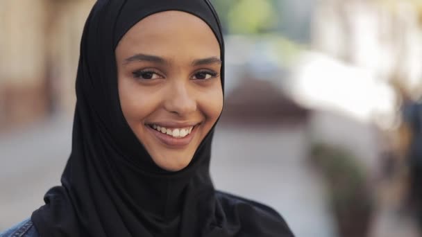 旧市街の背景に立つカメラに微笑むヒジャーブのヘッドスカーフを着た美しい若いイスラム教徒の女性の肖像画. — ストック動画