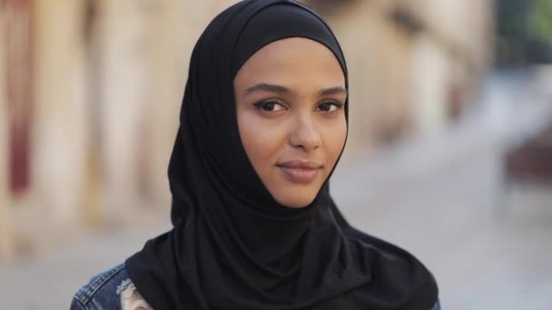 Retrato de una hermosa joven musulmana con pañuelo en la cabeza hijab sonriendo a la cámara de pie sobre el fondo de la vieja ciudad . — Vídeos de Stock