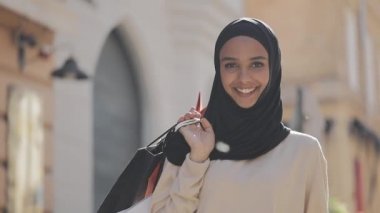 Elinde alışveriş çantaları ile sokakta ayakta hijab mutlu genç Müslüman kadın portre. Online alışveriş, alışverişkolik kavramı.