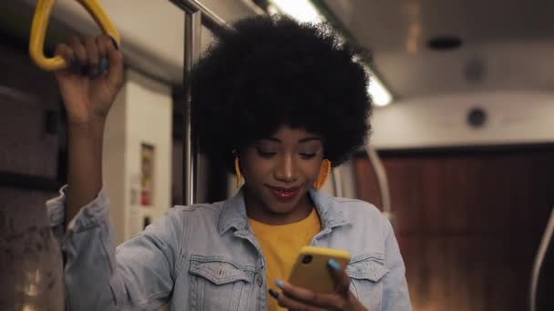 Atractiva mujer afroamericana joven sostiene la barandilla y el uso de teléfonos inteligentes en el transporte público. Tiempo nocturno . — Vídeo de stock