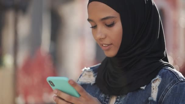 Jeune belle femme musulmane utilisant smartphone debout sur le fond de la vieille ville. Elle a de bonnes nouvelles sur smartphone . — Video