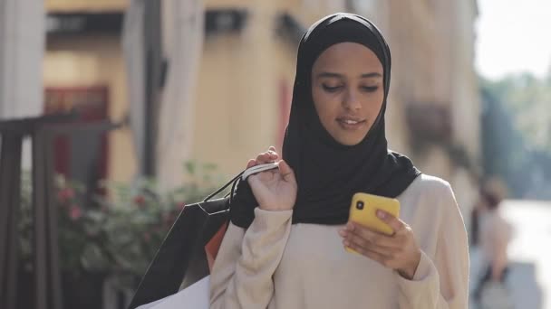 Joven musulmana en hijab caminando por la calle con bolsas de compras en la mano. Shopaholic, concepto de compras por Internet . — Vídeo de stock