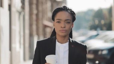 Takım elbiseli ciddi bir Afro-Amerikan iş kadınının portresi, şehirde dolaşıp, kahve içerken ve kameraya bakmak. Konsept: yeni iş, iş günü, serbest.