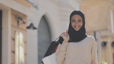 Elinde alışveriş çantaları ile sokakta ayakta hijab mutlu genç Müslüman kadın portre. Online alışveriş, alışverişkolik kavramı.