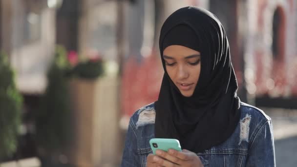 Wanita muslim muda yang cantik menggunakan smartphone berdiri di latar belakang kota tua. Dia punya kabar baik di smartphone . — Stok Video