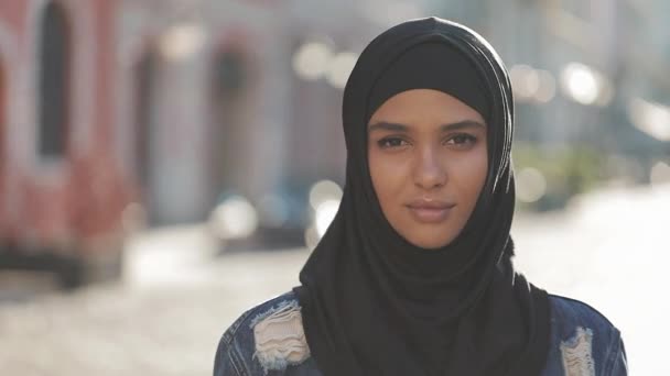 Porträt einer schönen jungen Muslimin mit Hijab-Kopftuch, die vor dem Hintergrund der Altstadt in die Kamera blickt. — Stockvideo