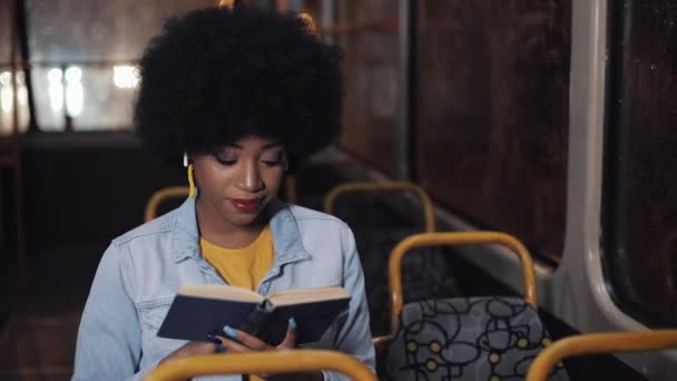 Mladá africká americká žena nebo osobní četba, která sedí ve veřejné dopravě, střela ze steadiamu. Zpomaleně. Pozadí světel města. — Stock video
