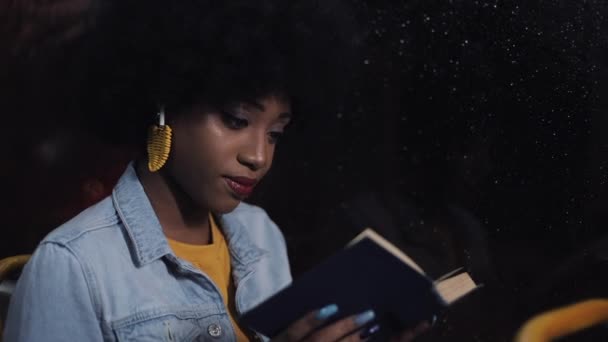 Giovane donna afroamericana o passeggero lettura libro seduto nei trasporti pubblici, colpo steadicam. Al rallentatore. Luci della città sfondo . — Video Stock