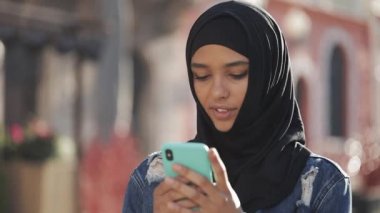 Genç güzel Müslüman kadın eski şehir arka plan üzerinde duran akıllı telefon kullanarak. Akıllı telefonda iyi haberleri var..