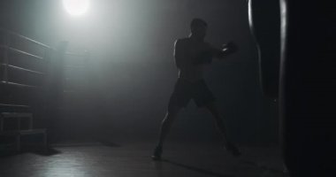 Siluet boksör adam karanlık spor salonunda kum torbası vurur. Dövüşçü egzersizi. Erkek boksör karanlıkta egzersiz. Kickboxer siluet eğitimi.