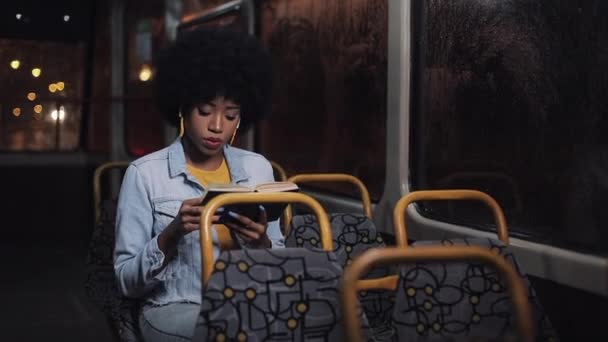 Genç afro-amerikan kadın veya yolcu okuma defteri toplu taşıma oturan, steadicam vurdu. Yavaş çekim. Şehir ışıkları arka plan. — Stok video