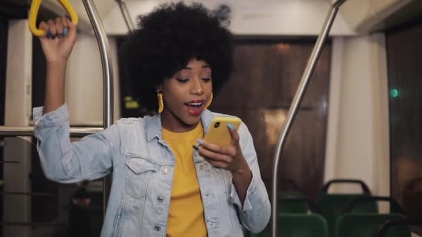 Feliz afro empresária aplaudindo celebrando olhando para o smartphone. Jovem mulher de negócios bem sucedida profissional urbana recebendo boas notícias equitação no transporte público . — Vídeo de Stock