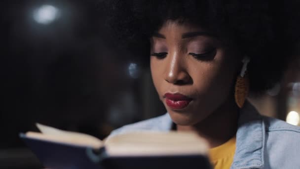 Joven afroamericana mujer o pasajero lectura libro sentado en el transporte público, steadicam disparo. En cámara lenta. Ciudad luces fondo . — Vídeo de stock