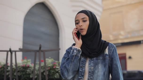 Όμορφη νεαρή μουσουλμανική γυναίκα φορώντας κασκόλ κεφάλι μαντίλα πηγαίνει στο παλιό κέντρο της πόλης και συνομιλίες στο τηλέφωνο. — Αρχείο Βίντεο