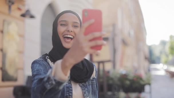 Retrato de una joven musulmana usando hijab haciendo videollamadas usando la cámara mientras viaja por la bella ciudad . — Vídeos de Stock