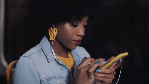 Attractive young african american woman using smartphone riding at public transport. Night time. City lights background. — Stock Video