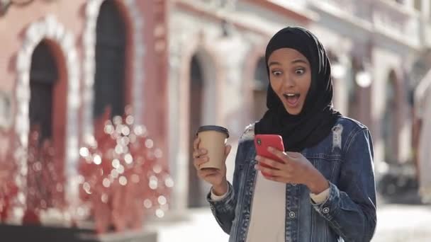 Joven mujer musulmana hermosa usando teléfono inteligente caminando sobre el fondo de la ciudad vieja. Ella tiene buenas noticias en el teléfono inteligente . — Vídeos de Stock