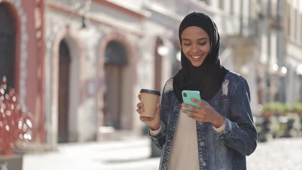 Wanita muslim muda mengenakan jilbab berjalan di pusat kota, menggunakan smartphone dan minum kopi. Komunikasi, belanja online, konsep jejaring sosial . — Stok Video