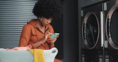 Çamaşırhanede akıllı telefon kullanarak gülümseyen genç kadın. Self-Servis kamu Çamaşırhane.