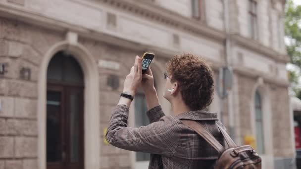 Hipster chico con gafas tomando fotos en su teléfono de la cámara que viaja por Europa. Turista hombre tomando fotos con la cámara del teléfono fuera . — Vídeo de stock