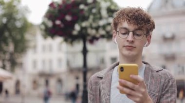 Sosyal ağlarda arkadaşlarınızla sohbet ve şehir sokakta yürürken modern akıllı telefon cihazını kullanarak müzik dinlemek, gözlük ile genç hipster adam. Kentsel yaşam tarzı.