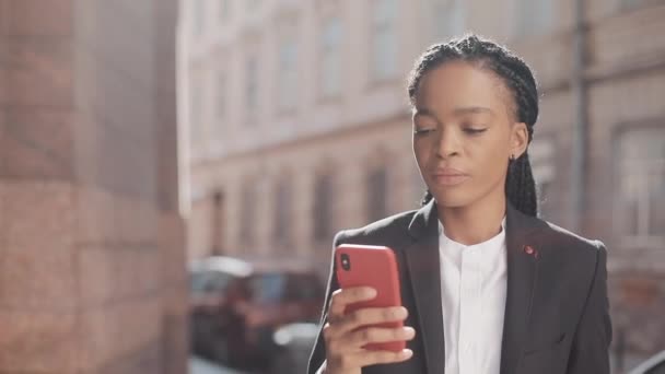 Стильна афро ділової жінки, використовуючи смартфон ходьбі по вулиці недалеко від бізнес-центру. Чорний стильний. Дреди. Афро зачіска. — стокове відео