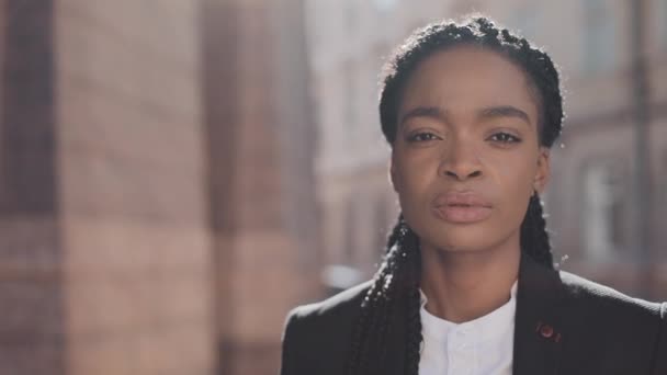 Portret van serieuze Afro-Amerikaanse zakenvrouw staande op de oude straat in de buurt van Business Center. Ze kijkt naar de camera en glimlacht. Zwarte stijlvolle. Dreadlocks. Afro kapsel. — Stockvideo