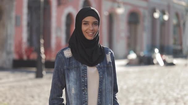 旧市街の背景に立つカメラに微笑むヒジャーブのヘッドスカーフを着た美しい若いイスラム教徒の女性の肖像画. — ストック動画