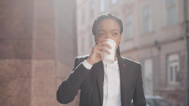 Portret van een serieuze Afro-Amerikaanse zakenvrouw in een pak, wandelen door de stad, en koffie drinken. Concept: nieuwe Business, werkdag, freelancer. — Stockvideo