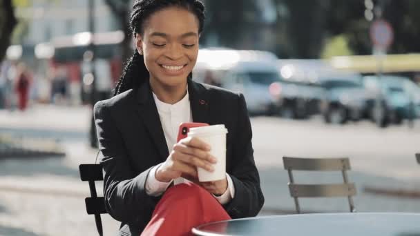 Femme d'affaires afro élégant utilisant smartphone boire du café assis sur la terrasse d'été dans un café confortable. Communication, travail, concept de réseau social . — Video