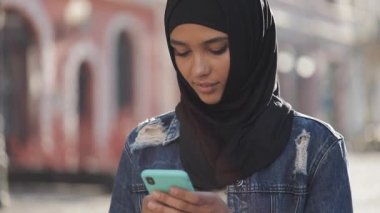 Genç güzel Müslüman kadın eski şehir arka plan üzerinde duran akıllı telefon kullanarak. Akıllı telefonda iyi haberleri var..