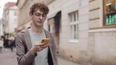 Sosyal ağlarda arkadaşlarınızla sohbet ve şehir sokakta yürürken modern akıllı telefon cihazını kullanarak müzik dinlemek, gözlük ile genç hipster adam. Kentsel yaşam tarzı.