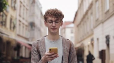 Sosyal ağlarda arkadaşlarınızla sohbet ve şehir sokakta yürürken modern akıllı telefon cihazını kullanarak müzik dinlemek, gözlük ile genç hipster adam. Kentsel yaşam tarzı.