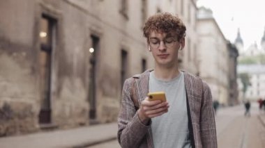 Sosyal ağlarda arkadaşlarınızla sohbet ve şehir sokakta yürürken modern akıllı telefon cihazını kullanarak müzik dinlemek, gözlük ile genç hipster adam. Kentsel yaşam tarzı.
