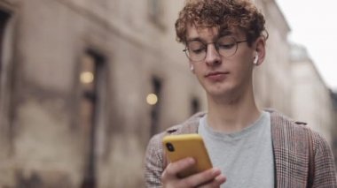 Sosyal ağlarda arkadaşlarınızla sohbet ve şehir sokakta yürürken modern akıllı telefon cihazını kullanarak müzik dinlemek, gözlük ile genç hipster adam. Kentsel yaşam tarzı.