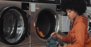 Genç Afro-Amerikalı kadın bir çamaşır makinesi önünde oturur ve çamaşırları götürmek. Self servis kamu çamaşırhanesi.