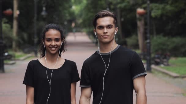 Πορτρέτο του νεαρού Καυκάσιος άνθρωπος και Μούλιν γυναίκα φορώντας ακουστικά που αναζητούν χαρούμενη στέκεται στο πάρκο άνθρωποι concept. — Αρχείο Βίντεο