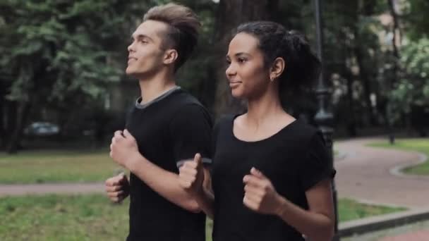 Joven pareja caucásica mirando emocionada usando trajes de correr sonriendo y charlando corriendo en el parque concepto estilo de vida saludable vista lateral . — Vídeo de stock