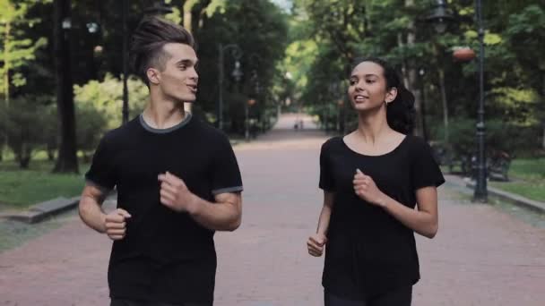 Barátok fiatal férfi és női looking izgatott mosolygó kidding viselése a jogging öltönyök futás a parkban Concept egészséges életmód. — Stock videók