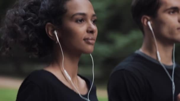 Bonito jovem Couplel em Headphones Looking Relaxed Running in Park Vista lateral Close Up Concentre-se na menina . — Vídeo de Stock