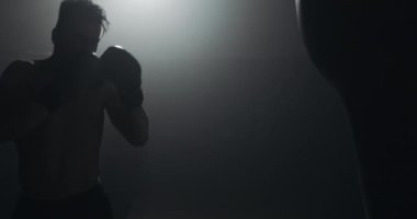Siluet boksör adam karanlık spor salonunda kum torbası vurur. Yakın savaşçı egzersiz. Erkek boksör karanlıkta egzersiz. Kickboxer siluet eğitimi.