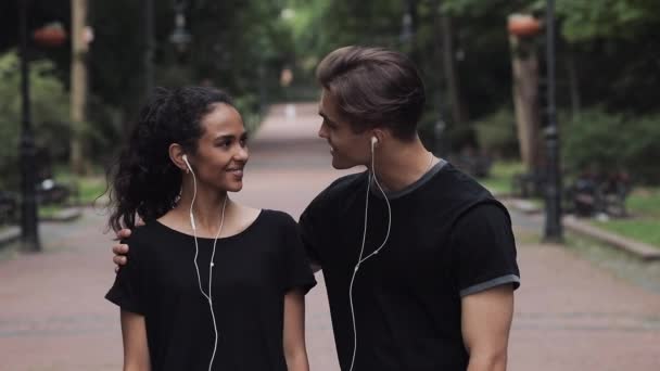 Atractiva Musline Girl y el hombre joven con los auriculares hablando sonriente hombre le da un abrazo amistoso en Park Slow Motion . — Vídeo de stock