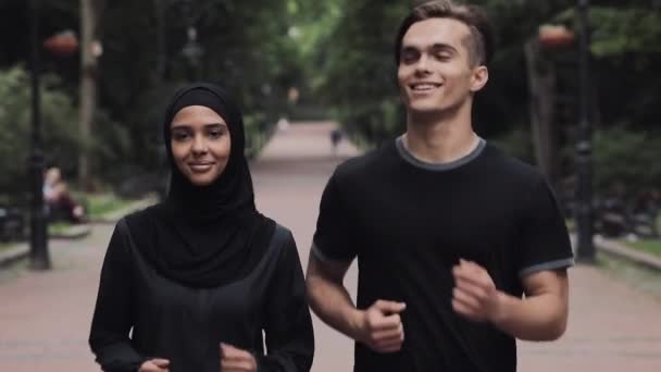 Young Caucasian Man and Muslin Women Wearing Hijab Looking Excited and Relaxed Smiling and Chatting Running in the Park Close Up. — Stock Video